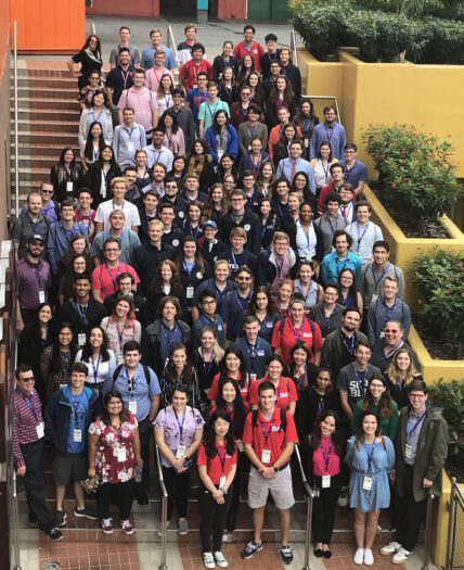 a diverse group of about 120 students at RITDC 2019 pose standing on a staircase at Universal CityWalk for a group photo, taken from a balcony